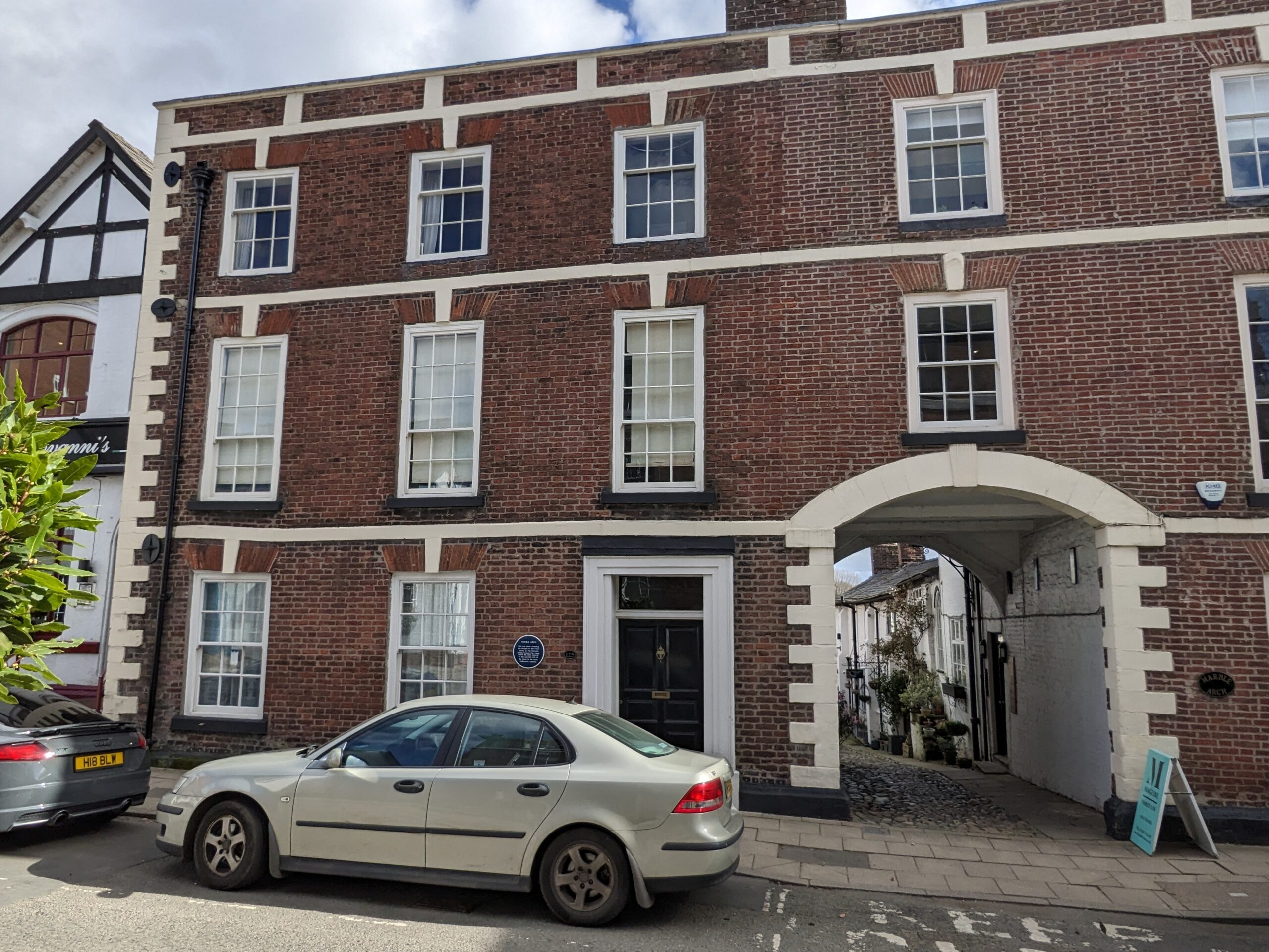 a red brick building with white panelled windows and an arch way leading into a colourful courtyard.